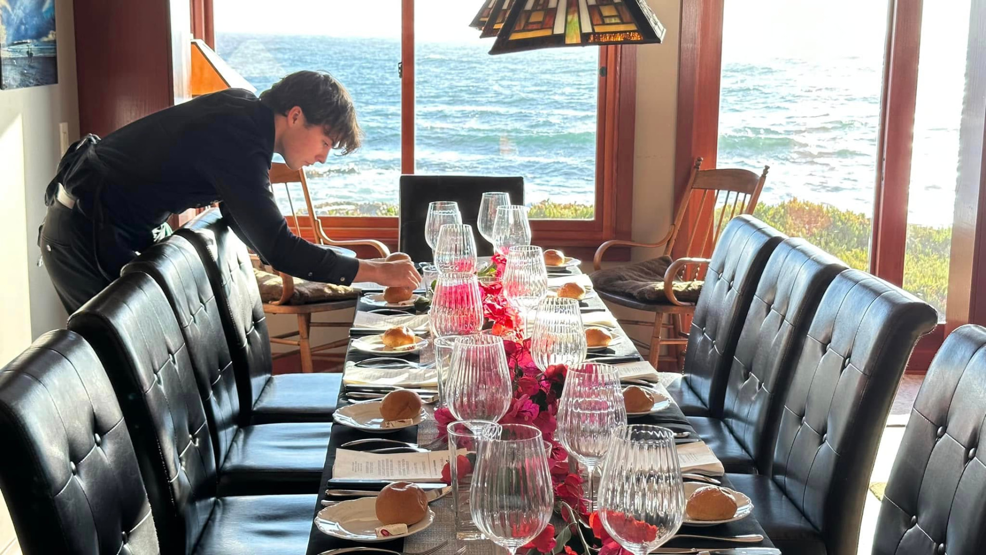 Long dining table set with crystal glassware beside ocean windows